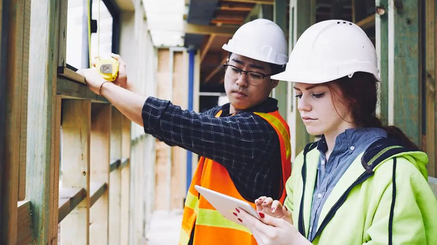 Two workers at a construction site, one using a tablet to perform a digital inspection